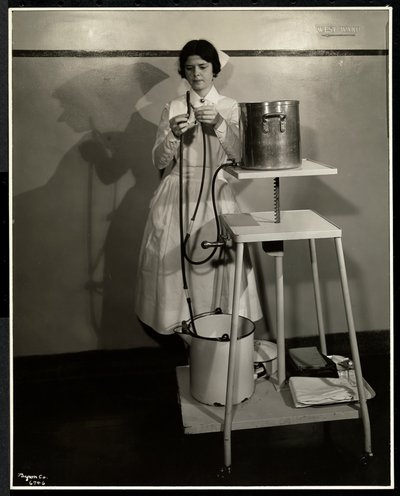 A nurse demonstrating a special apparatus with tubes and supply and refuse buckets at Sloan Maternity Hospital, Broadway and 168th Street, New York, 1932 by Byron Company